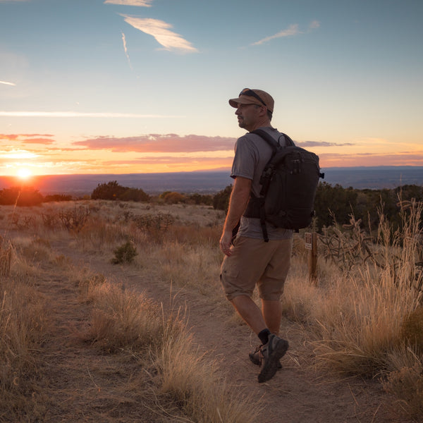 Man with a backpack walking on a dirt path during sunset in a desert landscape